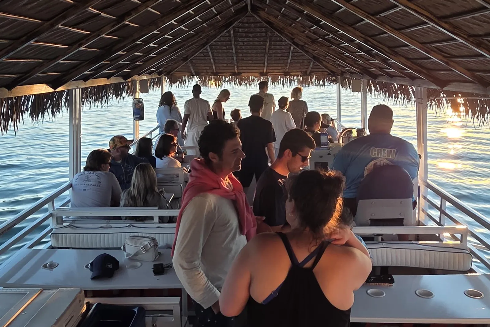 Guests gathered under the thatched roof with the water and a low sun behind them